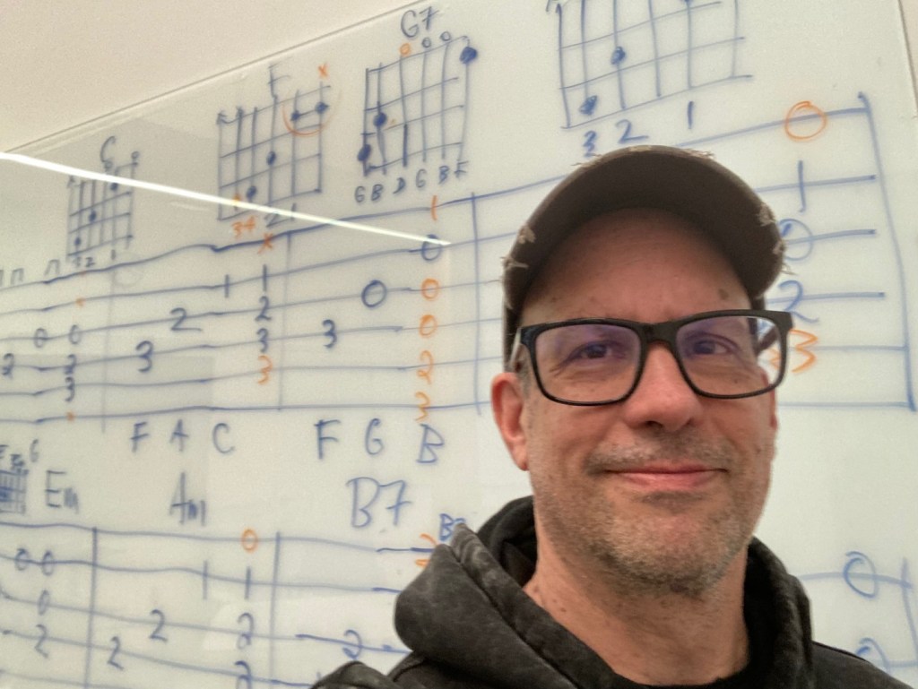 Dave teaching a group guitar class to seniors at the City of Redmond with whiteboard chord symbols and TAB in the background.